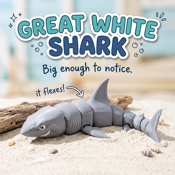Great White Shark 3D printed articulated flexi toy by Cosmic 3D Creations, on sand with driftwood and shells