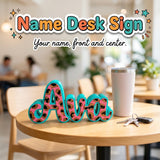 Name Desk Sign 3D printed personalized standing sign with the sample name Ava in leopard print by Cosmic 3D Creations, on a cafe table