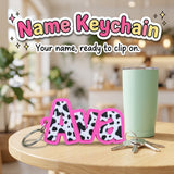 Name Keychain 3D printed personalized keychain with the sample name Ava in cow print by Cosmic 3D Creations, on a cafe table