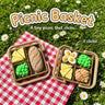 Picnic Basket 3D printed clicker fidget toy by Cosmic 3D Creations in two styles, with a bread loaf and with deviled eggs and a croissant, on a gingham picnic blanket
