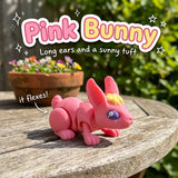 Pink Bunny 3D printed articulated flexi toy by Cosmic 3D Creations, on a sunny garden table with flowers