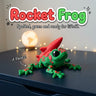 Rocket Frog 3D printed articulated flexi toy by Cosmic 3D Creations, on a desk with star lights