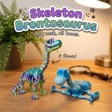 Skeleton Brontosaurus 3D printed articulated flexi toy by Cosmic 3D Creations, on a wooden desk with a fern