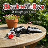 Skunk with Rose 3D printed articulated flexi toy by Cosmic 3D Creations, on a sunny garden table with flowers